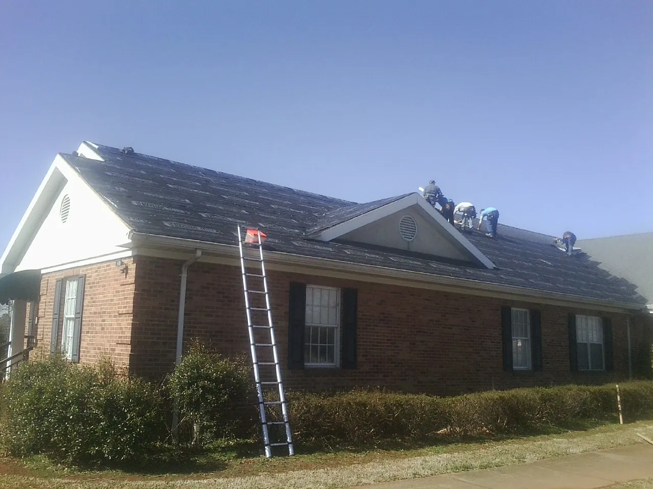 Crew tearing shingles off a brick ranch roof with a ladder set — Emergency Roof Repair work by our crew in Donegal