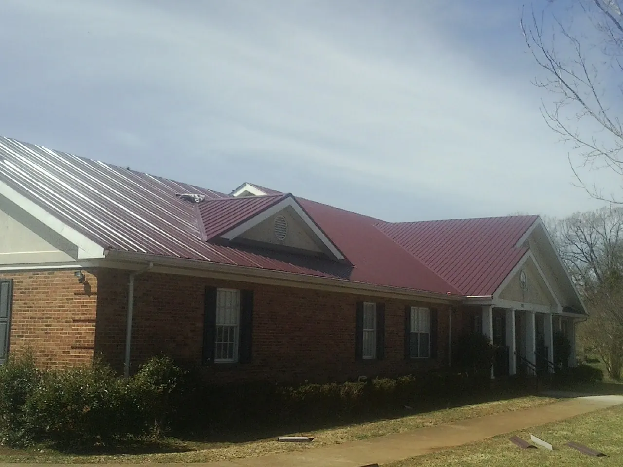 Red metal roof with gabled entries on a long brick building, from a Hail Damage Roof Repair job in Donegal