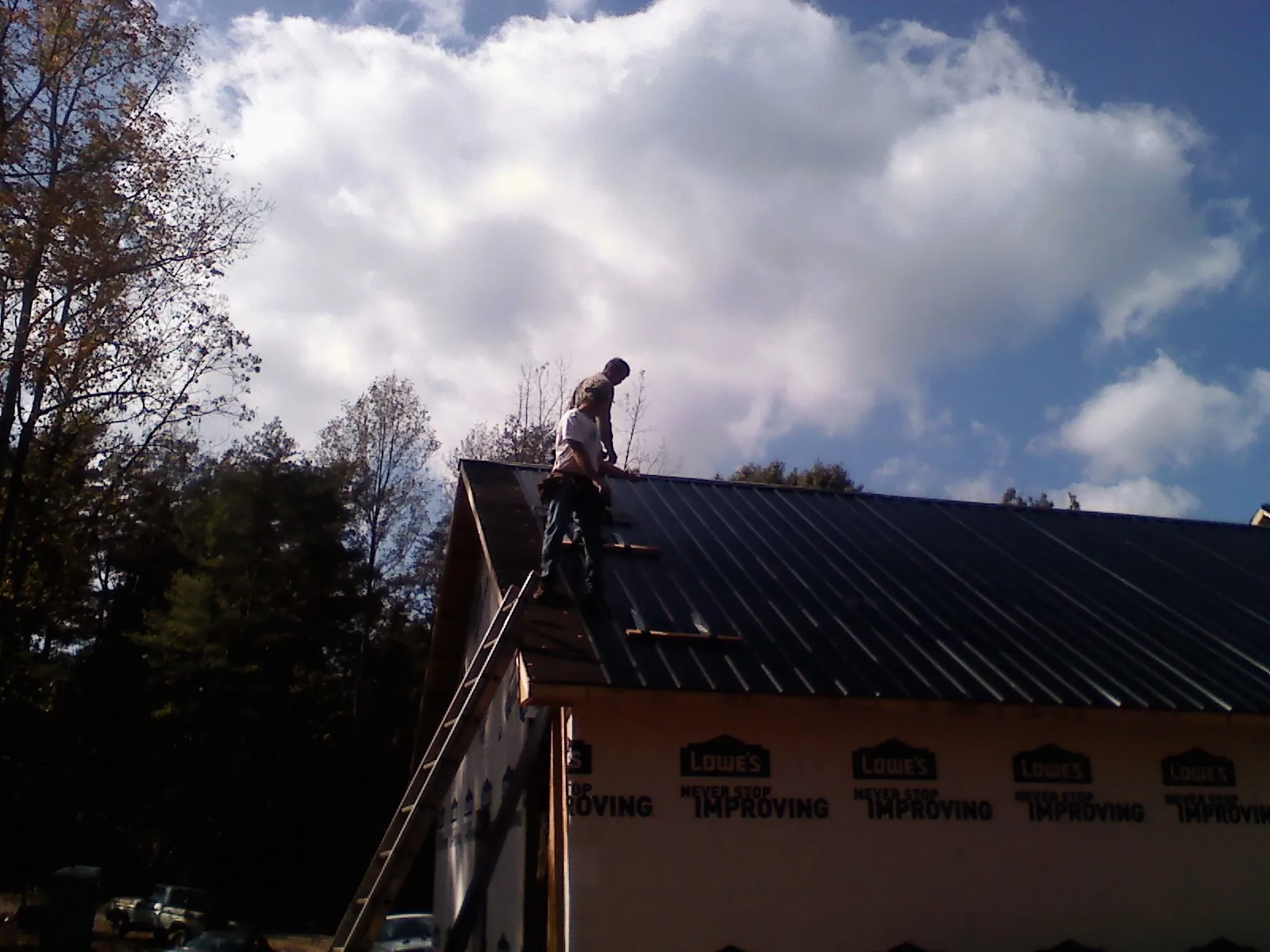 Roofer fastening dark metal panels high against a cloudy sky, from a Roof Inspection job in Donegal