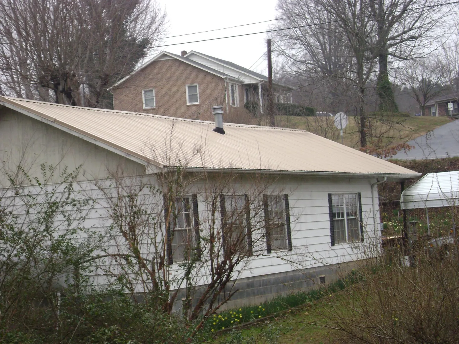 Tan metal roof on a white sided house set into a hillside — Commercial Roofing by Roofing Brothers in Donegal